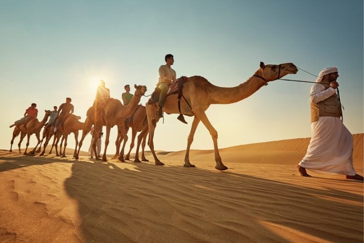 Persone che esplorano il deserto di Abu Dhabi sui cammelli