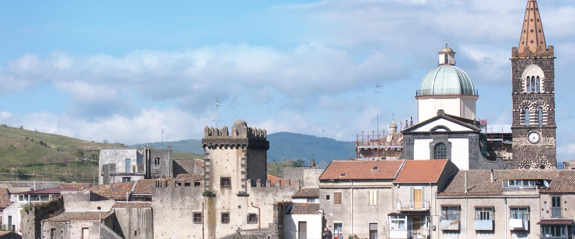 Vista della città di Randazzo, Sicilia, con una torre medievale merlata, case con tetti rossi e la chiesa di San Martino con la sua cupola e campanile.